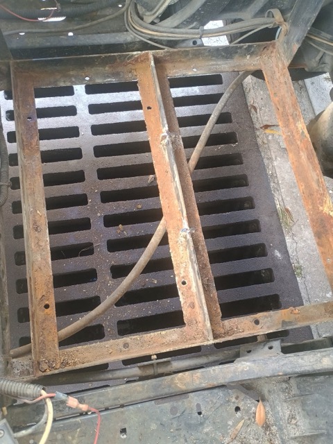 The cart’s existing metal battery tray frame, with visible rust, above a slotted floor and a cable.