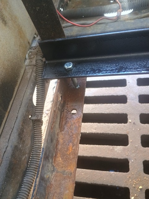 Close-up of a hex bolt fastening a black mounting rail to the rusted tray frame.