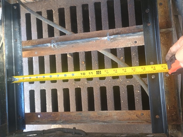 Two black mounting rails placed across the rusted tray, with a tape measure stretched between them.